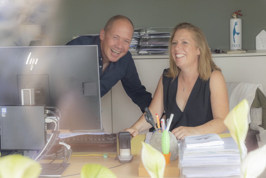 Die Geschwister Elmar und Aiga Sautter, beide CEO von disana lachend am Schreibtisch schauen in die Kamera