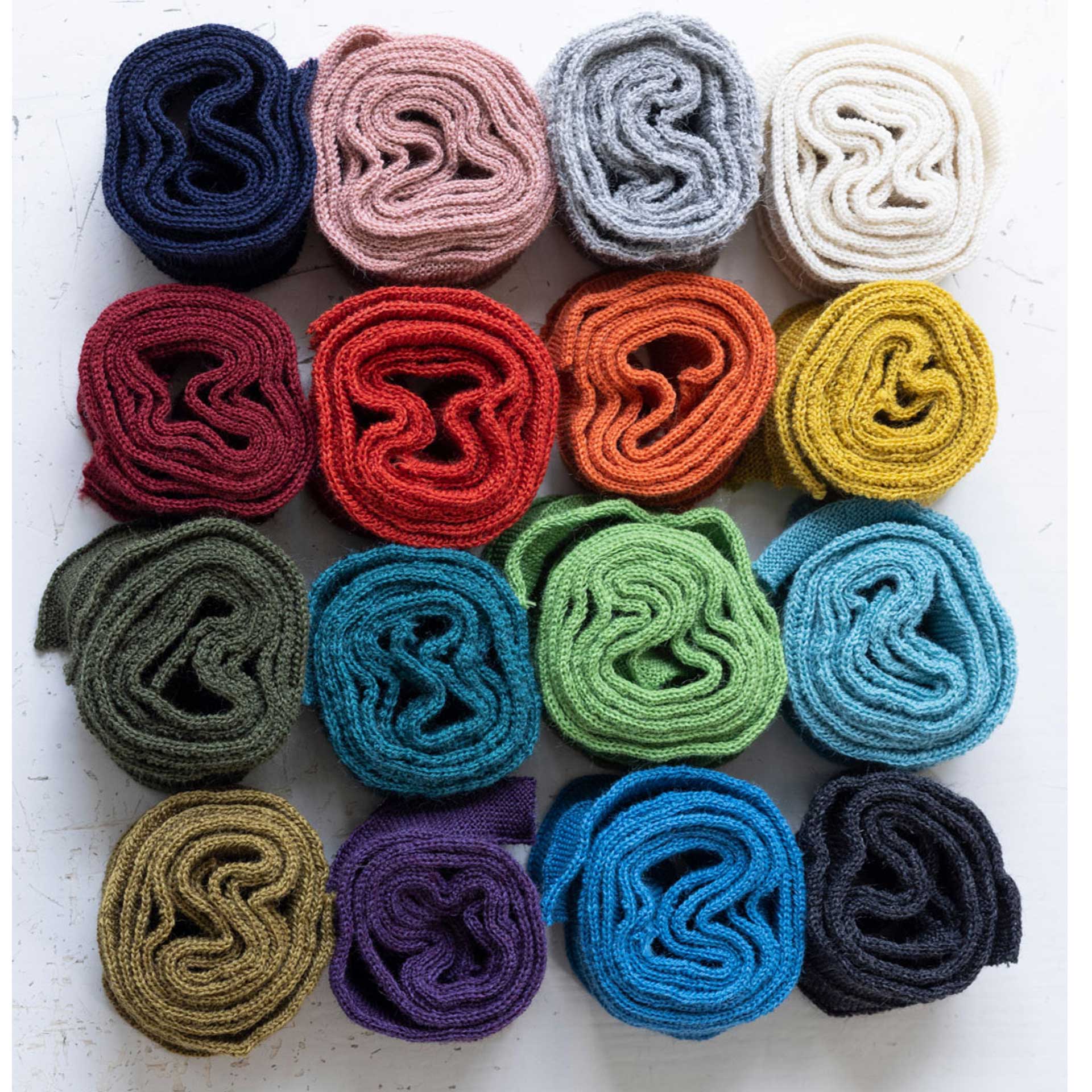 Verschiedene farbige Einfassbänder von disana aus Wolle, gerollt und dekorativ angeordnet. Ideal als Ersatzteil für Reparatur